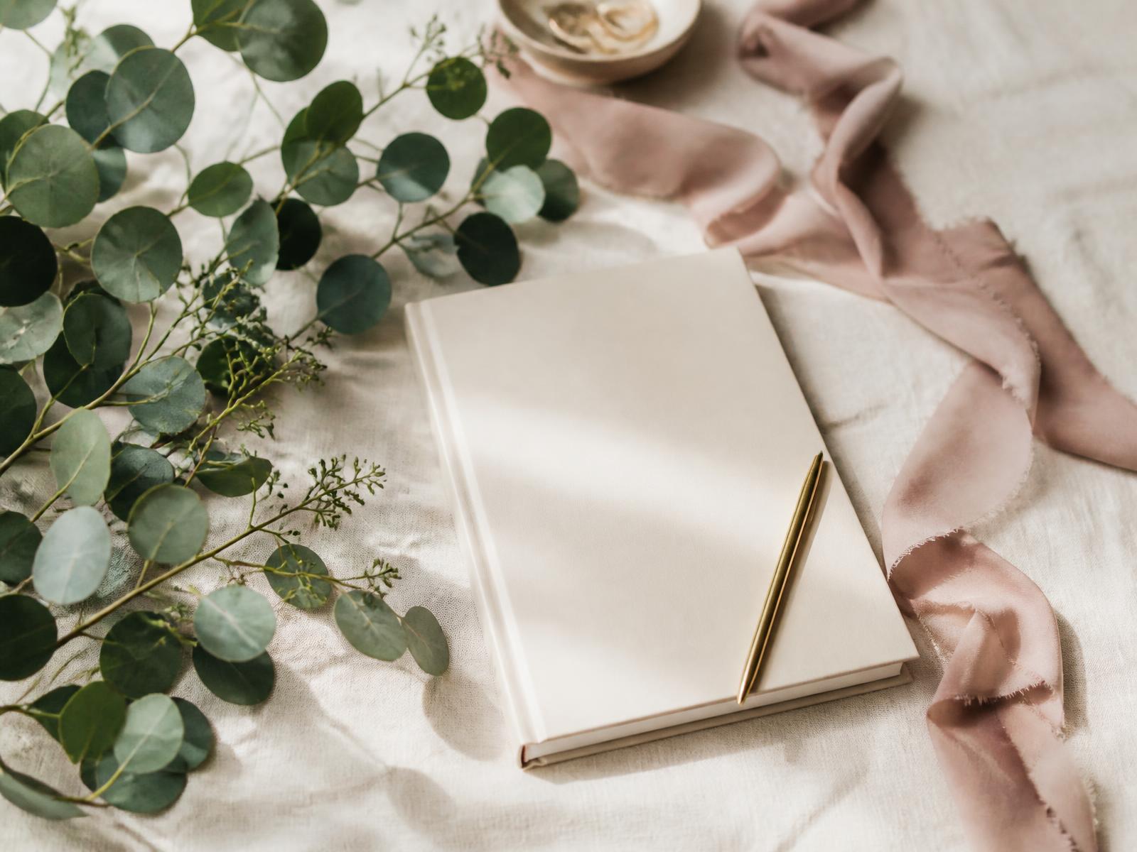 Cream linen with eucalyptus, a dusty rose ribbon and a wedding planning notebook